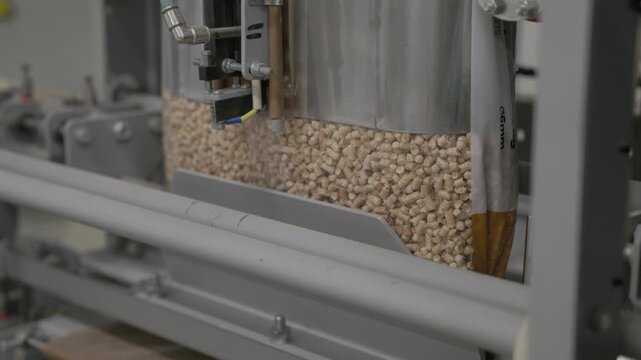 Wood pellets being packed into a clear bag inside automated industrial packaging machinery