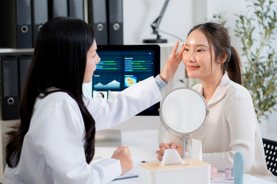 Asian woman doctor touching face of patient in clinic and discussing skin analysis on computer screen with ai technology, dermatologist examining facial beauty and consultation for health skin care.