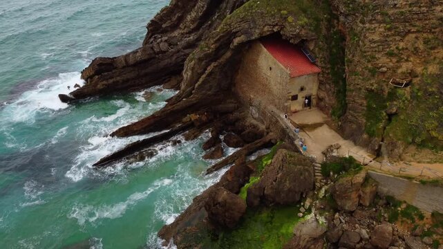 Aerial drone view of Santa Justa Hermitage, a unique chapel built inside a coastal cliff cave in Ubiarco, near Santillana del Mar, Cantabria, Northern Spain. High quality 4k footage