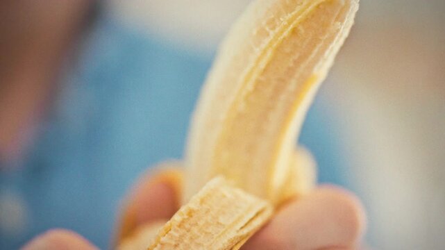 A close-up of a man's hands slowly peeling a fresh yellow banana, revealing the tender, juicy flesh with its natural texture. Healthy eating concept in a sunny kitchen