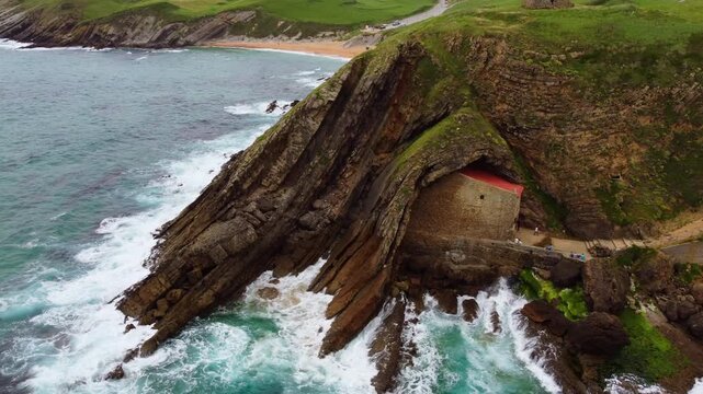 Aerial drone view of Santa Justa Hermitage, a unique chapel built inside a coastal cliff cave in Ubiarco, near Santillana del Mar, Cantabria, Northern Spain. High quality 4k footage