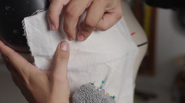 Close-up of pinning muslin fabric onto dress form for bespoke wedding gown construction