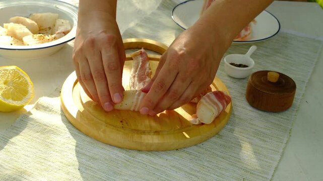 A chef wraps strips of raw cod in thinly sliced ​​bacon for grilling. Step-by-step video recipes. Horizontal video.