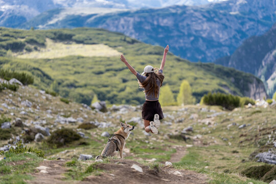 Woman jumping joyfully on mountain trail with her dog, hiking freedom and celebration concept