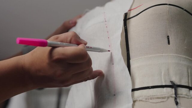 Fashion designer drawing pattern lines on pinned muslin fabric over dress form during couture dressmaking