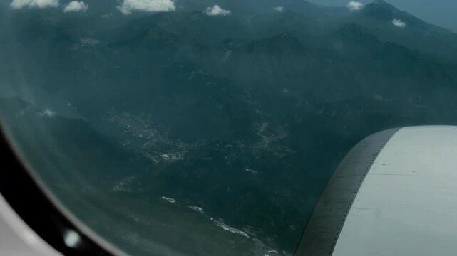 Passenger plane window seat view flying over deep mountain valleys and hills