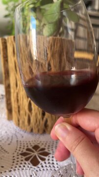 A close-up of a young woman enjoying a drink, symbolised by her holding a glass of red wine and swirling it.