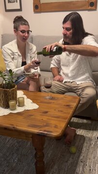 Young woman and mid-adult man enjoying a glass of red wine and conversation while relaxing on a sofa in a comfortable and cozy living room