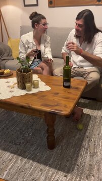 Vertical view of a young woman and a mid-adult man enjoying a casual and relaxing evening at home, drinking red wine