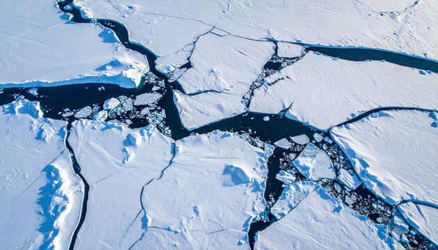 Abstrakte Luftaufnahme von oben auf massives arktisches Packeis, brillante schneewei&szlig;e Eisschollen mit tiefen Rissen im mitternachtsblauen Ozeanwasser, hoher Kontrast