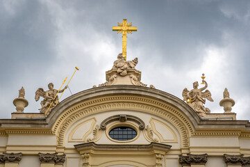 Baroque church in Warsaw with gilded cross, angels and ornate facade under dramatic spring sky © Luis