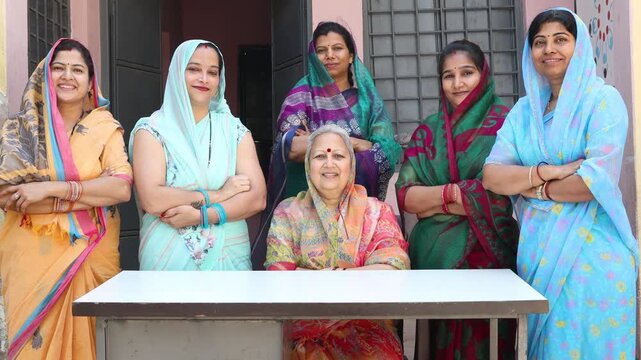 Group of happy indian women wearing traditional saree standing together looking at the camera, community spirit and female empowerment. Rural india.
