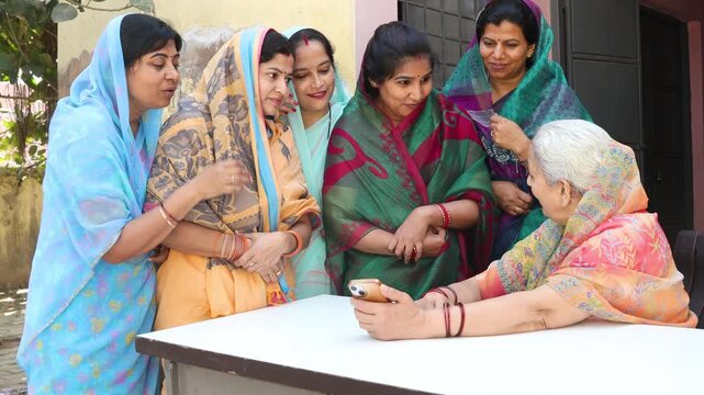 Group of indian women gathering around an elderly woman using smart phone, community learning digital literacy social awareness and education in rural india. Government scheme. Female empowerment.