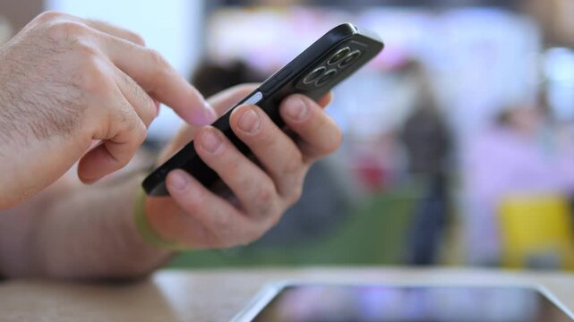 Close-up of hands using a smartphone. Fingers tap screen with focus. Background blurred with indistinct people. Suitable for tech, communication, or mobile usage themes