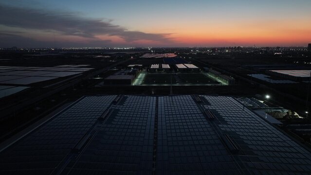 Industrial factory rooftop solar panels under twilight sky with city lights in the distance