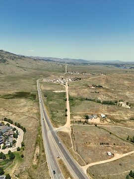 Aerial view of a highway intersection surrounded by dry, rolling hills and sparse vegetation under a clear blue sky in Boulder, Colorado, United States.