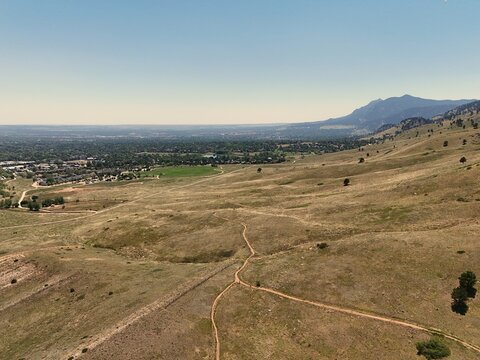 Aerial view of Fourmile Canyon Creek Trailhead area featuring rolling grassy foothills, dirt hiking trails, and the distant city skyline in Boulder, Colorado, United States.