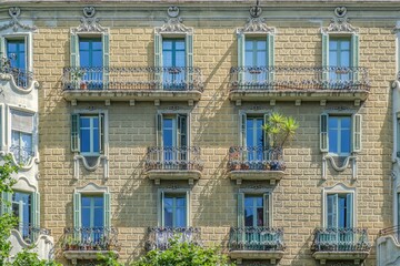 Fototapeta premium Facade with Green Windows and Balconies in Barcelona, Wrought Iron Railings, Historic Apartment Exterior