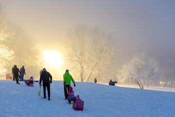 Naklejka premium Family and friends enjoying winter sledding at sunset on a snowy hill with frosty trees