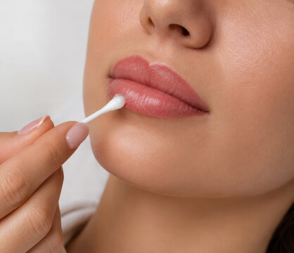 Woman cosmetologist applying moisturizing cream on lip of young woman after permanent makeup procedure. Professional lip tattoo care and recovery in beauty studio. Skincare treatment.