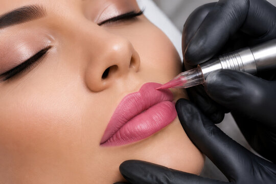 Permanent makeup artist performing lip tattoo procedure on young woman. Professional cosmetic micropigmentation technique to enhance lip shape and color. Beauty salon skin care treatment.