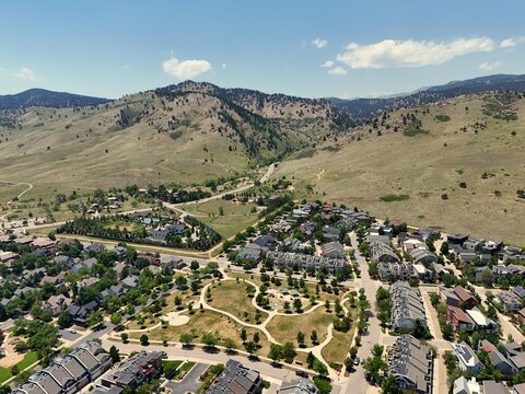 Aerial view of a residential neighborhood with a central park, winding walking paths, and modern houses nestled against the foothills of the Rocky Mountains in Boulder, Colorado, United States.
