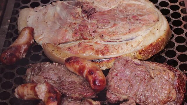Pork belly, beef steaks, and sausages grilling on the barbecue, with a barbecue fork and smoke.