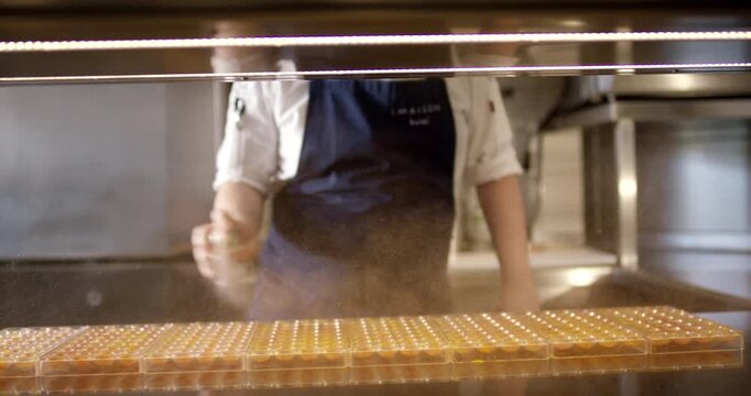 Baker using a hand spray bottle to mist water or glaze over rows of small pastries