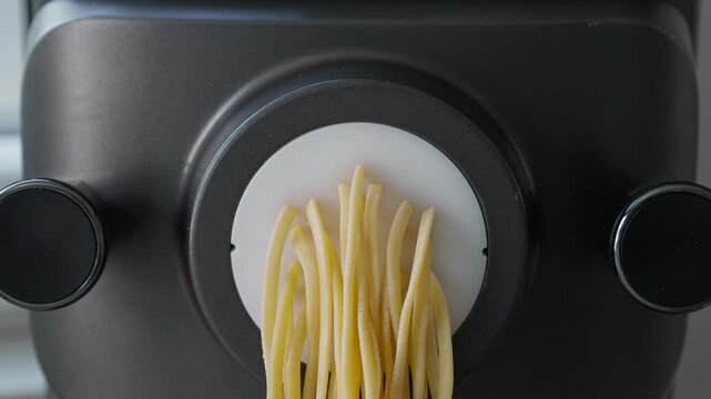 Fresh egg pasta coming out of a pasta machine during homemade cooking preparation, closeup