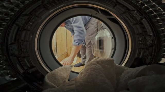 A man in the laundry room loads soiled garments into a washing machine, initiating a cleaning cycle amidst his domestic duties, managing household chores efficiently