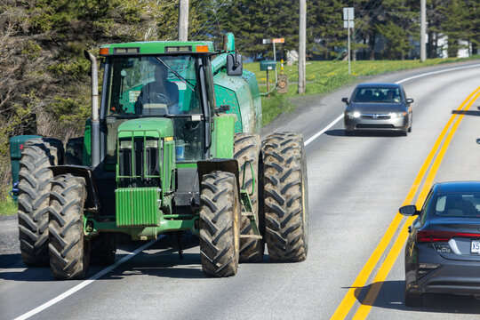 Gaspesie, Canada, 30 May 2026 : A green John Deere tractor drives on a paved road alongside passenger vehicles.