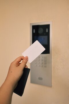 Hand holding an RFID card near an electronic access reader in a modern building. Suitable for concepts of security, access control, and smart building technology.