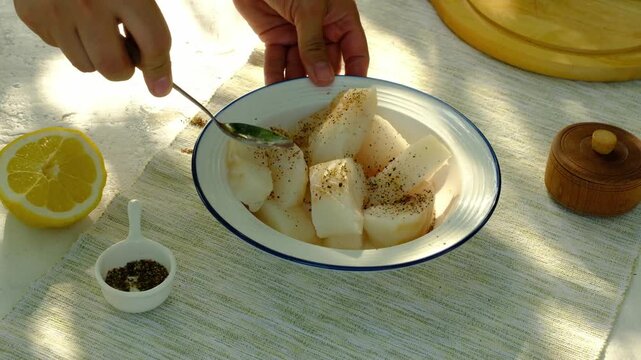 A chef seasons raw cod strips with ground pepper for grilling. Step-by-step video recipes. Horizontal video.