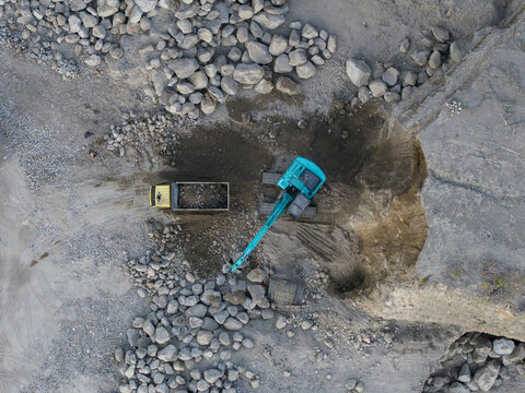 Aerial view of an excavator loading rocks into a dump truck at a sand and stone quarry in Manisrenggo, Central Java, Indonesia.