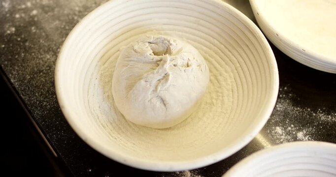 Close-up of a baker placing a shaped piece of bread dough into a round proofing basket