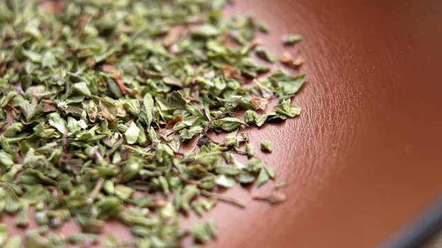 Crushed dried oregano (Origanum vulgare) spread across a rustic ceramic surface. Mediterranean culinary herb. Organic herbal seasoning. Macro. Rotation