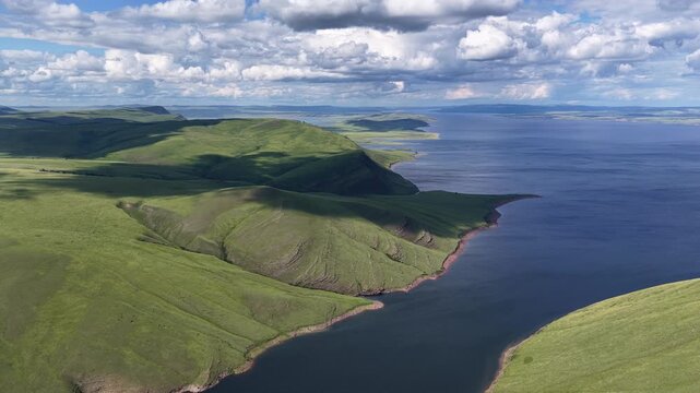 Scenic aerial view of rolling green hills, rugged coastline, and deep blue water under a cloudy sky in summer. Universal natural landscape, concept of ecotourism, freedom, and wilderness.
