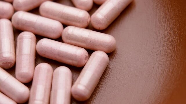 Fingers picking pink gelatin vitamin B12 capsule from a heap of dietary supplements