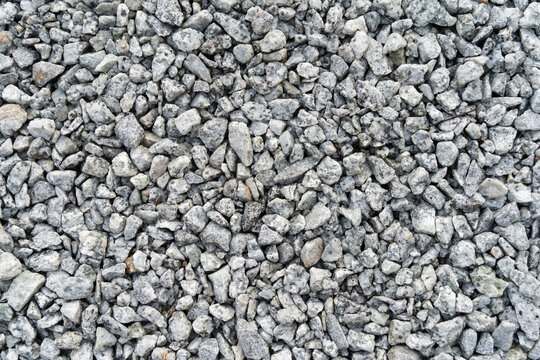 A close-up of crushed gray gravel stones forming a rough, textured surface, commonly used for construction, landscaping, and road foundations.