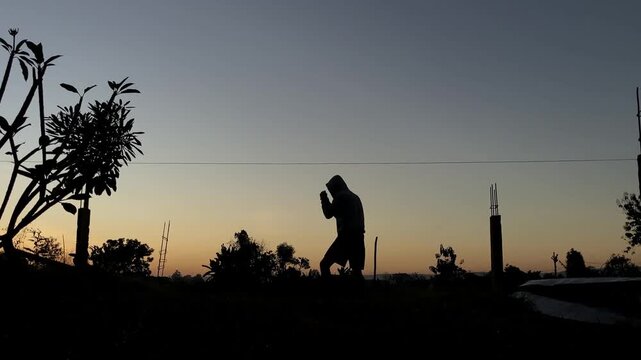 Silhouette of Hooded Athlete Practicing Muay Thai High Kick at Dusk