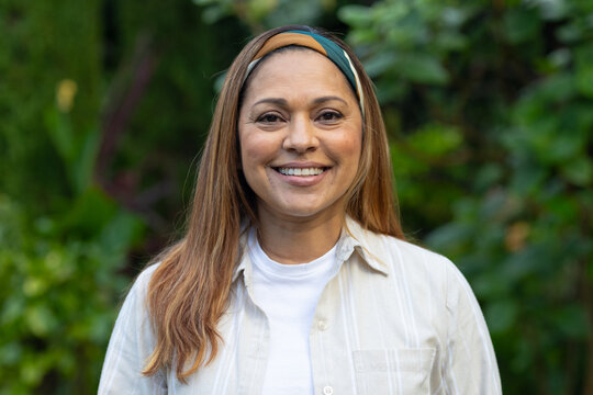Mature African American woman standing, smiling in yard wearing bright headband beige top white tee