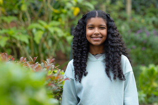 African American youth female standing smiling in garden in pale blue hoodie and black hair clips