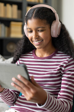 African American teenage female sitting on couch with pink headset and maroon top holding tablet