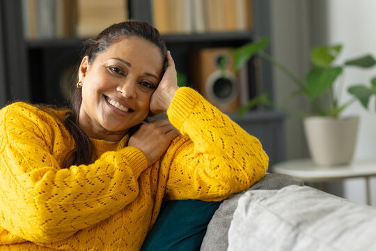 Mature African American woman leaning on sofa with cushion in living room, wearing yellow sweater