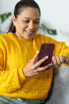 African American woman in yellow sweater holding burgundy phone and checking watch on couch