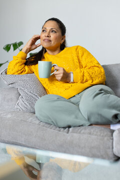 Mature African American woman reclining on gray sofa, wearing yellow sweater, holding mint mug