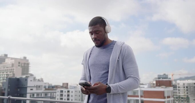 Mid-30s man tapping phone, starting music listening and dancing on rooftop terrace with headphones