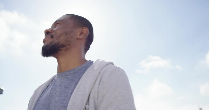 Mid-adult African man in light gray zip hoodie turning left smiling, reacting to sun on rooftop