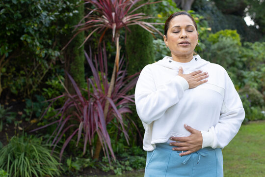 African American woman practicing breathing in garden with white hoodie and blue pants, copy space