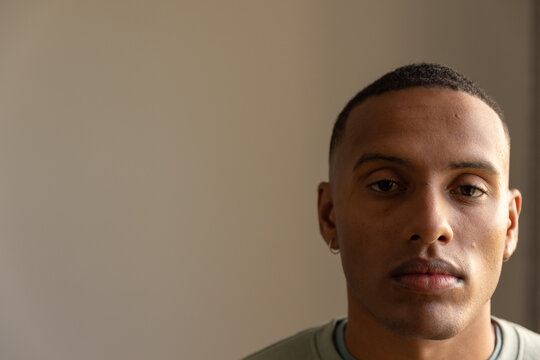 African American man posing in room with beige wall wearing green shirt, hoop earring, copy space